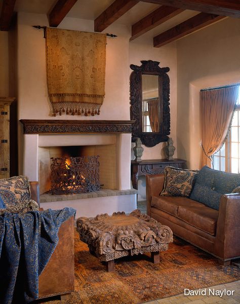 This Afghan Bhokara rug, in a rare shade of saffron, inspired the room. The coffee table is a repurposed column top. An embroidered French tapestry hangs above a fireplace shielded by an antique French screen. The mirror frame and mantel were carved in the Visions workshop. Santa Fe Interior Design, Santa Fe Interiors, Mexico Hacienda, Hacienda Home, Old World Interiors, Kiva Fireplace, Easy Decor Ideas, Hacienda Homes, Above Fireplace