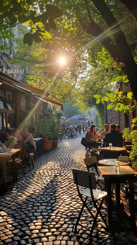 Sunlit Cobblestone Alley: A serene sunlit alleyway with people enjoying outdoor dining on a beautiful cobblestone street. #sunlight #alley #cobblestone #dining #outdoor #trees #city #cafes #aiart #aiphoto #stockcake https://ayr.app/l/ic7K City Trees Street, Italian Cobblestone Street, Alleyway Restaurant, Parisian Patio, Urban Hiking, Cobblestone Street, Seaside City, Dining Outdoor, Walkable City