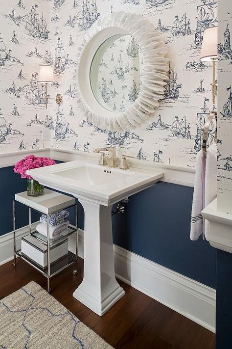 White and navy powder room features top half of walls clad in white and blue ship print wallpaper and lower half of walls painted navy blue finished with a thick chair rail. Navy Powder Room, Bathroom Wallpaper Nautical, Blue Powder Rooms, Bathroom Chair, Chair Rail Molding, Powder Room Wallpaper, Classic White Kitchen, Pedestal Sink, Chair Rail