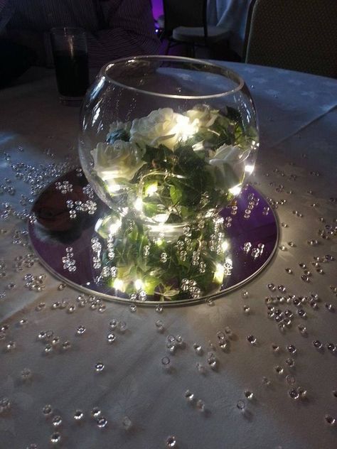 6 inch fishbowl centrepiece on mirror plate with white silk rose ivy and purple lights. Mirror Plate Centerpiece, Rehearsal Table Decorations, Fishbowl Decor, Prom Centerpieces, Outdoor Micro Wedding, Fishbowl Centerpiece, Geometric Terrarium Wedding, Mirror Centerpiece, Terrarium Centerpiece