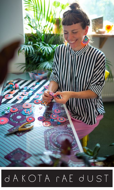 Jewellery designer Bec is sitting at a desk scattered with colourful patterned discs. The desk has a blue and purple pattern on it and a pair of pliers are seen next to the discs. She is wearing a black and white striped shirt and large, colourful teardrop shaped earrings. She is looking down focusing on the circular patterned earring component she is hand stitching and smiling. In the background a large house plant is visible. Art Jewellery Design, Fabric Bead Earrings, Textile Necklace Wearable Art, Scrap Fabric Earrings, Textile Jewellery Handmade, Textile Jewelry Diy, Fabric Jewellery Handmade, Fabric Jewelry Diy, Fabric Jewelry Necklace