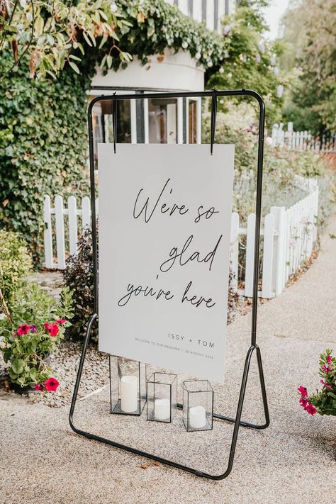 Black and white wedding welcome sign on black metal frame with pillar candles in vases for minimal and classic style wedding Welcome Sign Wedding 2023, Clothes Rail Wedding Sign, Cloth Wedding Signs, Hanging Wedding Welcome Sign, Black And White Wedding Welcome Sign, Simplistic Wedding Decor, Wedding Welcome Table Ideas, Wedding Welcome Boards, Unique Wedding Welcome Sign