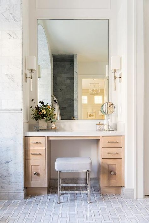 A gray leather seat sits on gray maze floor tiles at a blond wood makeup vanity adorned with polished nickel pulls and a white quartz countertop fixed beneath a tall mirror lit by Hudson Valley Lighting Taunton Wall Sconces. Vanity Nook, Vanity In Bathroom, Dressing Vanity, Wood Makeup Vanity, Makeup Vanity Decor, Design Hall, Vanity With Mirror, Dressing Table Design, Vanity Drawers