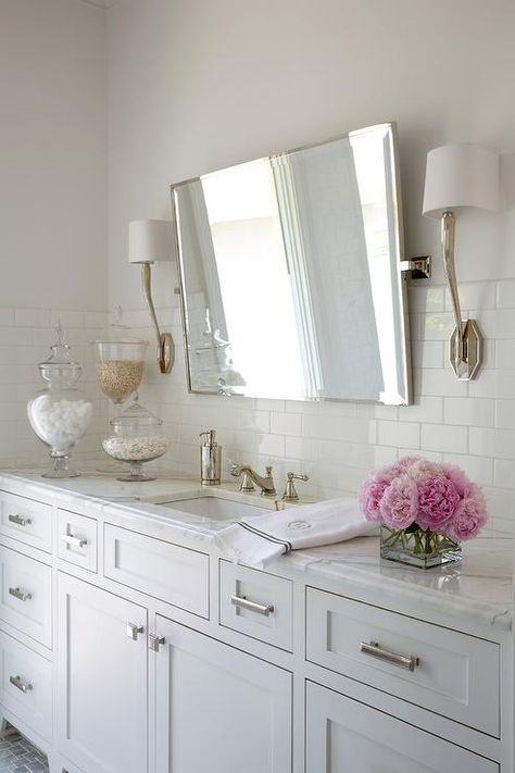 Ruhlmann Single Sconces flank a rectangular pivot mirror fixed against a half tiled wall over a white shaker washstand donning polished nickel pulls and a white quartz countertop holding a polished nickel faucet over a rectangular sink. White Countertop Bathroom, Exchange Of Energy, Pivot Mirror, Polished Nickel Faucet, White Countertop, Countertop Bathroom, Bubble Bubble, White Quartz Countertop, Local Furniture