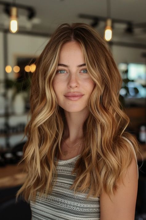 Woman with long wavy blonde hair and a striped top smiling indoors with blurred lights in the background. Golden Brown Hair Honey Caramel Highlights, Toffee Blonde Hair Caramel, Carmel Highlights On Brown Hair Light, Balayage On Strawberry Blonde Hair, Gigi Hard Hair, Caramel Macchiato Hair Color, Highlights For Ginger Hair, Fall Highlights For Light Brown Hair, Warm Hair Color Ideas Blonde