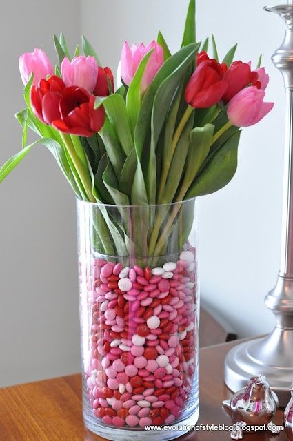 Centerpiece for a Valentine's tablescape. Tulip and valentine M's vase - place a smaller glass vase inside a larger one. Fill the gap with M & M's. Valentine Tablescape, Saint Valentin Diy, Valentines Bricolage, Flowers For Valentines Day, Valentine Centerpieces, Valentinstag Party, Small Glass Vases, Valentines Flowers, Sweet Valentine