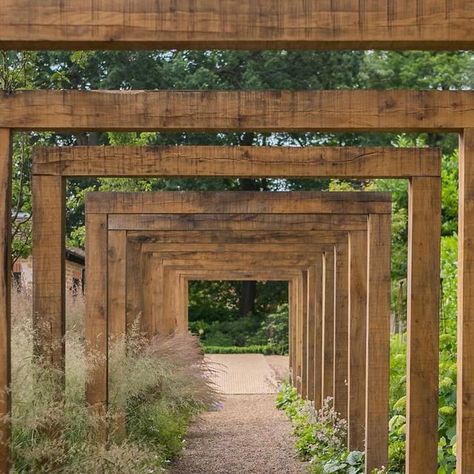 Studio Pollyanna on Instagram: "This Oak walkway was designed to draw you down into the garden, encouraging exploration away from the main dining space. The vertical structures balance the garden by adding height to the left side of the garden, complementing a brick wall that sits on the far right.  Subtle spike lights uplight the timber, and woodland planting flanks the path. 
Project location: Surrey" English Homestead, Woodland Planting, Timber Pergola, Wood Trellis, Landscape Inspiration, Timber Walls, Homestead Gardens, Courtyard Design, A Brick Wall