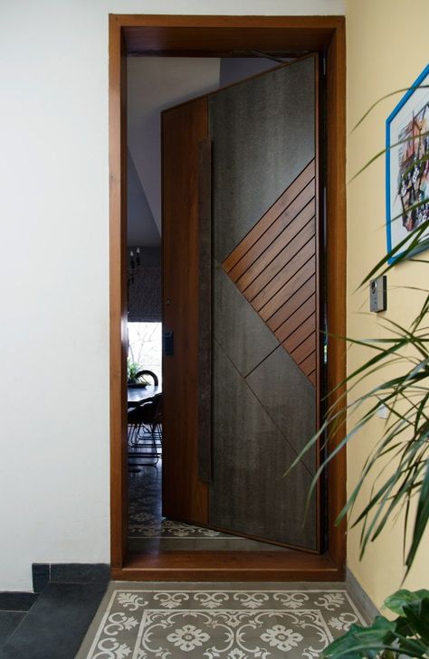 A subtle yellow wall leads to the main door of the house finished in stone and wood while the patterned tiles act as a faux rug. Photography by Prachi Damle Tor Design, Pintu Interior, Wooden Door Entrance, Flush Door Design, Modern Entrance Door, Modern Wooden Doors, Main Entrance Door Design, Front Door Design Wood, Wooden Front Door Design