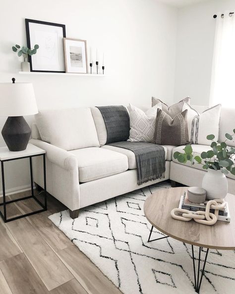 A white and black geometric rug gives a modern farmhouse feel to this modern living space. A wood coffee table with hairpin legs holds a wood chain garland with eucalyptus stems in a white vase. A white sofa with gray throws and neutral accent pillows fits into the corner. Gray Black And White Living Room Rugs, Corner Sofa With Coffee Table, Grey Couch With Black Accents, Cream Couch With Black Accents, Neutral Boho Living Room Grey Couch, Gray Black And Cream Living Room, White Couch Accent Pillows, Hearth And Hand Living Room, Ivory Sofa Living Room Decor