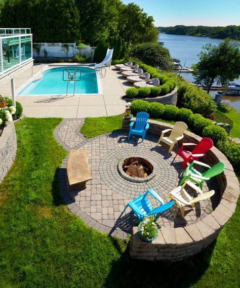 Overhead view of a dog and wood-burning round fire pit in the centre of a brick patio surrounded by colourful Adirondack chairs over looking a pool and a river. Fire Pit Gallery, Fire Pit Landscaping, Fire Pit Furniture, Patio Fire Pit, Backyard Pool Landscaping, Fire Pit Area, Fire Pit Designs, Diy Fire Pit, Backyard Pool Designs