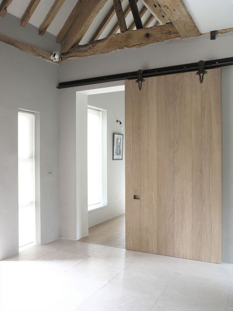 This large sliding barn door made from light wood and a dark metal rail creates a contemporary look in this remodeled home that maintained some of the original rustic ceiling details. Contemporary Barn, Industrial Apartment, Kitchens And Bedrooms, Barn Conversion, Modern Barn, Exposed Beams, Design Del Prodotto, Interior Barn Doors, The Ceiling