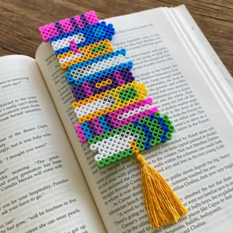 Here's another fun and useful project created from Perler fuse beads! It's a perfect little gift for any avid reader. Book Perler Bead Patterns, Perler Bead Gift Ideas, Book Perler Beads, Perler Bead Gifts, Perler Bead Book, Perler Bead Bookmarks Pattern, Hama Beads Bookmark, Perler Bead Bookmarks, Mini Perler Beads Ideas