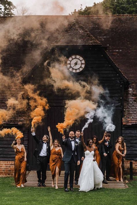 Bride in sweetheart neckline lace wedding dress with detachable off the shoulder sleeves, groom in classic black three piece grooms suit with bow tie and white rose and foliage boutonniere in church, bridesmaids wearing strappy sleeveless front slit burnt orange bridesmaid dresses holding foliage bouquets and groomsmen wearing classic black suits doing burnt orange and white smoke flares at Lains Barn wedding | Lee Daniels Photography Black And Wood Wedding Theme, Black And Rustic Orange Wedding, Black And Rust Wedding Colors, Burnt Orange Black Wedding, Black And Pumpkin Orange Wedding, Black And Orange Wedding Decor, Black Burnt Orange Wedding, Orange And Black Wedding Theme, Black And Orange Wedding Theme