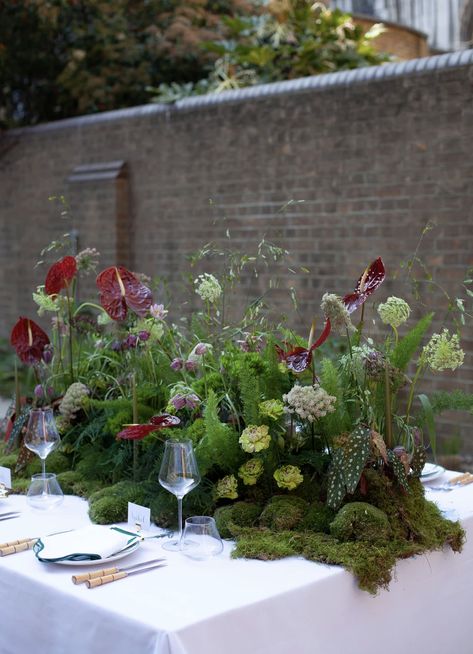 Moss base and woodland inspired stems. Al fresco dining Mossy Floral Arrangements, Woodland Table Scape, Moss Tablescape Wedding, Flowers For Dining Table, Woodland Dinner Party, Mushroom Floral Arrangement, Moss Christmas Decorations, Wedding Flower Installations, Moss Flower Arrangements