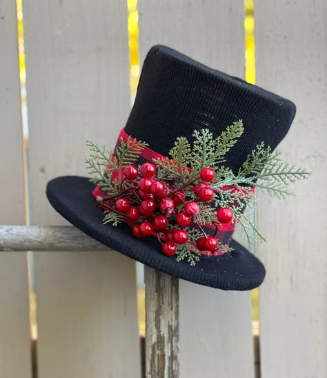 Eco-conscious materials are used in this product.  Materials include tin can, foam core, recycled hat, black paint, cotton ribbon, newly purchased varying holiday sprigs. holiday sprig vary with each product Can be used sitting or as a topper for a tree. Top Hat dimensions:    Brim of hat approximately 10 1/2 inches across                                          Top hat section is approximately 7 inches from brim to top                                         Opening in bottom of hat b\Brim is Recycled Hat, Diy Christmas Hats, Snowman Top Hat, Snowman Hats, Alice In Wonderland Props, Snowman Hat, Black Top Hat, Holiday Hats, Cotton Ribbon