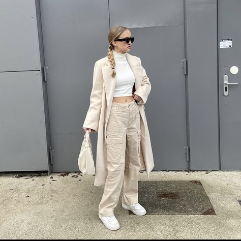 girl standing in front of a grey building wearing beige cargo pants, a white turtleneck, a beige oversized coat, a beige handbag and brown sunglasses How To Style Cream Cargo Pants, Chic Cargo Pants Outfit, White Cargo Pants Outfit Winter, Style White Cargo Pants, Beige Cargo Pants Outfit Winter, Cargo Pants Outfit Aesthetic, Fashion Trends Aesthetic, Beige Streetwear, Beige Cargo Pants Outfit