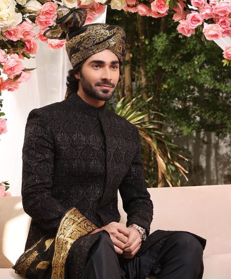 A classic black sherwani named "ADEL" from TABEER -E- KHAWAB. This timeless piece features self-embroidered fabric with a straight fit silk pyjama. Paired with a black turban embellished with golden weaving and a coordinating stole, creating a sophisticated monochrome look. The ensemble includes five pieces: Sherwani, kurta & pant set, turban, and stole. Materials include self-embroidered fabric for the sherwani, silk for the kurta & pants set, and silk for the turban. Ideal for grooms seeking a Pakistani Groom Outfits For Men, Black Sherwani Groom Pakistani, Black Sherwani Groom, Barat Outfit, Groom Indian Wedding Outfits, Dress Like Royalty, Black Sherwani, Black Turban, Regal Wedding