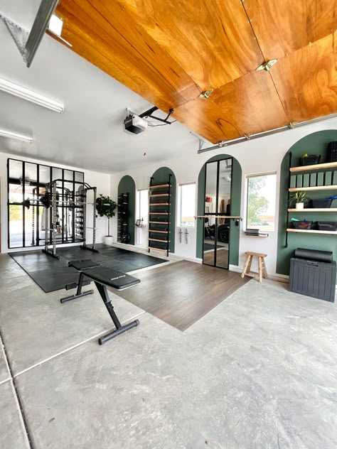 DIY home gym in a garage with green painted arches, large black framed mirror, a wall mounted weight rack, storage shelves, and ballet barre with dance floor. Gym Makeover Ideas, Garage Makeover Gym, Cute Garage Gym, Garage Ballet Studio, Garage Turned Into Gym, Garage To Gym Makeover, Yoga Studio Garage, Aesthetic Garage Gym, Garage Gym Corner