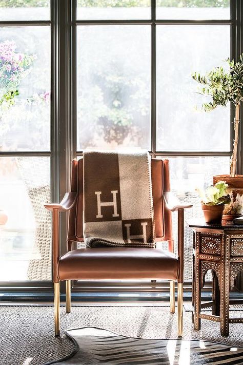 A brown Hermes Avalon throw blanket is draped over a brown leather accent chair placed in front of floor to ceiling windows and beside a brown Moroccan accent table. Hermes Throw Blanket Living Rooms, Hermes Home Decor, Hermes Interior Design, Hermes Throw Blanket, Hermes Interior, Hermes Decor, Brown Leather Accent Chair, Luxury Unboxing, Chair Blanket