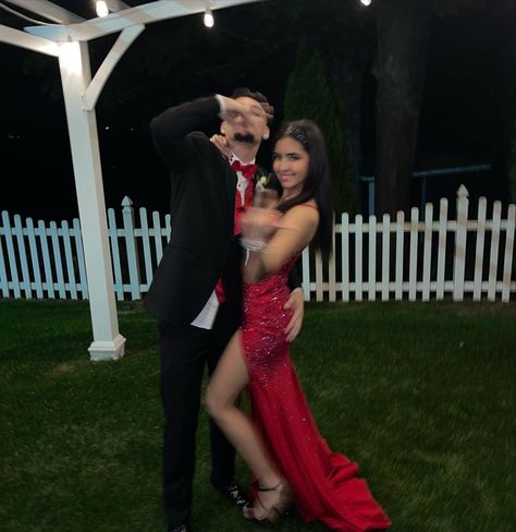 Two young adults posing for a photo at senior prom dressed in red. Guy is wearing a black suit with red vest and bow tie and making hand gesture over his face. Girl is wearing sparkly red dress with high slit and black heels. hair is styled with gems in a half slicked half out hairstyle. Red Prom Dress And Tux Ideas, Red And Black Prom Couples, Red Prom Couple Outfit, Red Prom Dress Makeup, Red Prom Couple, Prom Ideas Pictures, Matching Prom Outfits, Couple Prom Outfits, Red Prom Dress Sparkly