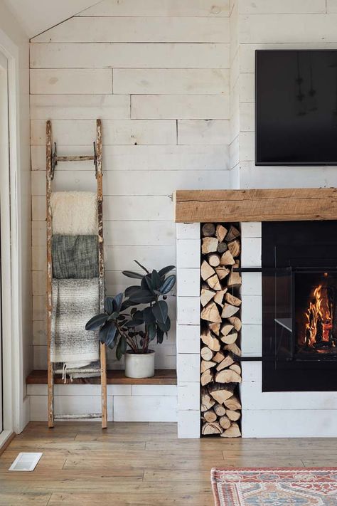 Revamp your fireplace mantel with a farmhouse-inspired look like this one in Kate and Tony Becker’s Corcoran home. Using barn wood adds character and charm, while throwing a blanket ladder, shiplap panels, and built-in firewood holder into the mix ties a simple, stylish aesthetic into your home. Photo by Wing Ta. Fireplace With Space For Wood, Blanket Ladder Fireplace, Blanket Ladder Next To Fireplace, Wood Holders For Fireplace, Fireplace Blanket Ladder, Built In Wood Box Next To Fireplace, Wood By Fireplace, Wood Holder In Fireplace, Firewood Storage Built In Fireplace