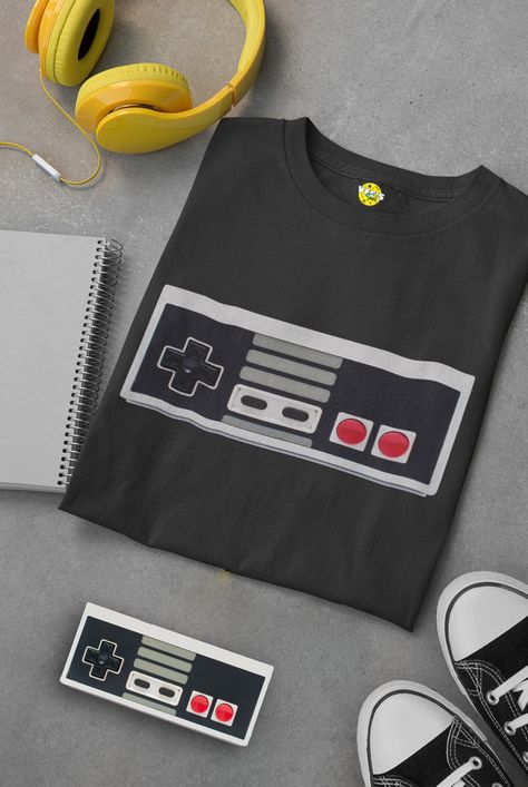 Step back into the golden age of gaming with our vintage NES controller short sleeve t-shirt. The iconic NES controller design on this tee is a true nostalgia trip for gamers of all ages. Relive your favorite gaming memories with this retro video game tee. Whether you're a seasoned gamer or just love the classic look, this shirt is a must-have addition to your collection. Level up your style with this NES controller t-shirt and show the world your love for classic gaming. It's not just a shirt; it's a piece of gaming history. Nes Controller, Gaming Tees, Controller Design, Retro Video, Retro Videos, Retro Video Games, Gaming Shirt, The Golden Age, Step Back