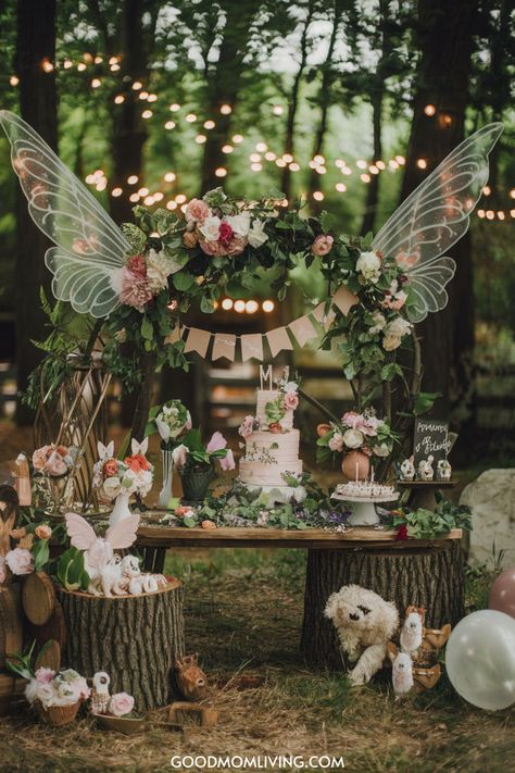 Whimsical outdoor birthday party setup featuring a decorated table with a floral arch, fairy wings, a multi-tiered cake adorned with flowers, and various themed decorations, all set against a backdrop of string lights and lush greenery. Enchanted Fairy Theme, Mushrooms And Fairies, Enchanted Forest Theme Quinceanera, Enchanted Mushroom Forest, Enchanted Forest Centerpieces, Fairy Wedding Theme, Enchanted Forest Theme Party, Enchanted Forest Quinceanera Theme, Enchanted Forest Quinceanera