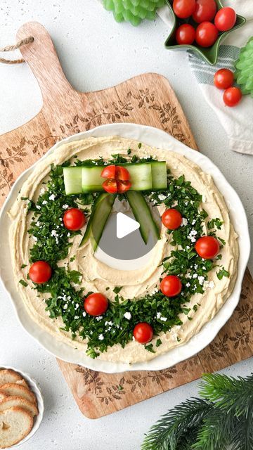 Kristel Talie on Instagram: "Christmas Hummus Wreath✨

Snack like Santa with this delicious hummus appetizer! I’m loving this Christmassy twist with tomato ornaments and a cucumber ribbon.. tasty and festive🌟🥰

You’ll need

Hummus (I used around 500g)
A small bunch of parsley finely chopped
Cherry tomatoes
Crumbled feta cheese
Cucumbers

1- Place a small bowl in the middle of your serving plate and evenly spread the hummus all around.
2- Remove the small bowl and top the hummus with chopped parsley, cherry tomatoes and feta.
3- Using a vegetable peeler, peel a few cucumber strips, form a Christmas ribbon as shown in the reel and place on top of the hummus. 
4- Serve with crackers or toasted bread. Enjoy!✨ 

#hummus #christmasfood #festivevibes #funfood #holidayfun #partyideas" Humus Christmas Wreath, Hummus Wreath Appetizer, Hummus Christmas Wreath, Christmas Hummus Wreath, Snack Ideas For Christmas Party, Xmas Cheese Board, Christmas Dinner Party Appetizers, Veggie Christmas Platter, Christmas Fruit Plate