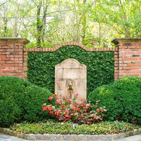 Here at Gardens to Love we take pride in making sure your garden is unique and special. This stone lion fountain among the sculpted bushes does a great job of illuminating the red brick behind it. Visit our website to learn all about the many features we could add to your space! #GardenstoLove #ATL Garden With Brick Wall, Walled In Garden, Brick Landscape Wall, Brick Walled Garden, Garden Features Focal Points, Garden Feature Wall, Brick Wall Garden, Garden Brick Wall, Brick Garden Wall