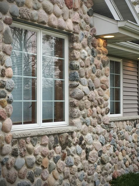 Granite veneer stone home shows Buechel Stone Granite Cobbles stone facade exterior stone veneer with siding. This residential natural stone install is in a fieldstone mosaic real stone pattern using mortar masonry (vs dry stacked stone) for a classic rustic cobbles look. See stone masonry blog post (https://www.buechelstone.com/masonry/) for more details on how to install stone veneer. #StoneVeneer #Fieldstone #StoneHome #StoneFacade #StoneCladding #ExteriorStoneVeneer #Masonry #GraniteVeneer River Rock Siding, Stone Facade House Exterior, Stone Facade Design, House Facade Design, Exterior Stone Veneer, Stone Siding Exterior, Purple Bedroom Design, Home Facade, Stone Veneer Exterior