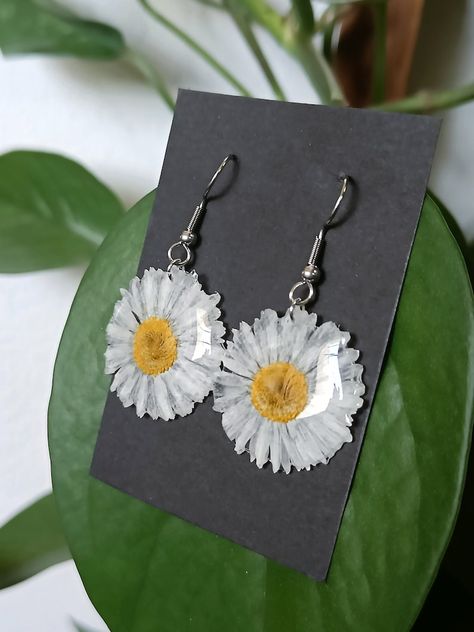 #Pendantearrings #handmade with real #Daisy #flowers dried in a #natural way and wrapped with #UVresin. They're an original #gift for a #naturelover or #perfect for a #bohostyle - #Daisyflowers symbolise #purity and #cheerfulness #innocence #positivity and #faithfullove but also #newbeginnings and #rebirth - #resinjewellery #daisyinresin #daisyearrings #earrings #dangleearrings #resinearrings #daisyjewellery #floraljewellery #botanicaljewellery #floralearrings #daisyresinjewellery #resin #gift Botanical Resin, Flowers In Resin, Daisy Pendant, Daisy Jewelry, Dangle Earrings Boho, Flowers Dried, Boho Style Jewelry, Daisy Earrings, Daisy Flowers