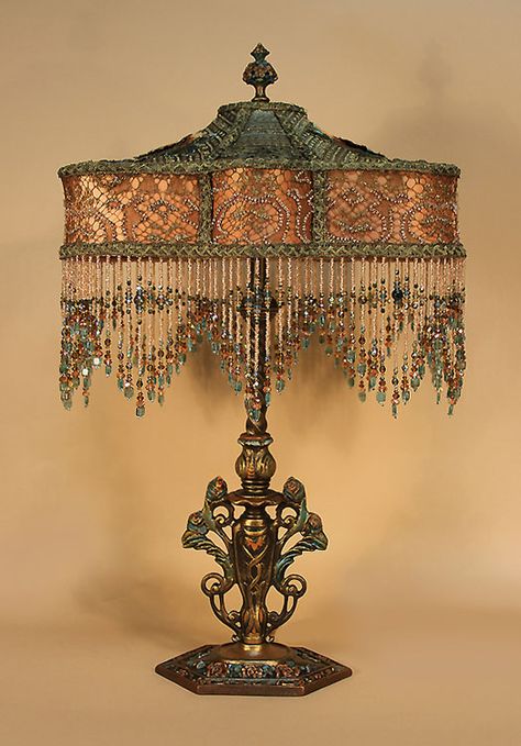 Ornate, painted metal table lamp holds a ‘KATIE’ shaped shade. Ombre dyed from teal blue into terra cotta and covered with gold metallic laces, the cuff is additionally embellished with a beaded pattern. The top is overlaid with two large silk embroidered roses in the same teal, gold and terra cotta tones. Hand beaded fringe Bohemian Victorian, Beautiful Lamps, Beaded Lampshade, Antique Lamp Shades, Victorian Table, Beaded Lamps, Witch Cottage, Victorian Lamps, Victorian Lampshades