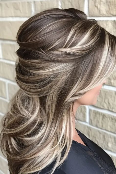 Woman with long, layered hairstyle featuring blonde highlights against a brick wall background. Dark Brown Light Brown And Blonde Hair, Best Hair Color To Camouflage Gray, Fresh Hair Color Ideas Brunettes, Mocha And Blonde Highlights, Hair Color Ideas For Brunettes Going Lighter, Partial Highlights For Brunettes Fall, Hair Color Ideas For Greying Hair, Hair Color To Cover Gray Hair, Mocha Latte Hair Color