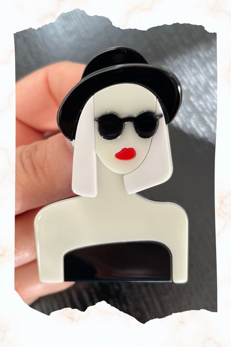 This stunning acrylic brooch is the perfect accessory to add some style and personality to any outfit. Featuring a unique design, this brooch showcases a beautiful woman wearing sunglasses and a hat The intricate details of the design are expertly carved into the acrylic, creating a stunning piece of wearable art. How To Make Brooches Handmade, Woman Wearing Sunglasses, Brooch Design, Wear Black Dresses, Hat Brooch, Acrylic Brooch, Art Deco Lady, Art Deco Brooch, Wearing Sunglasses