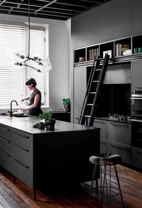 This [historic warehouse has been converted into an industrial-style apartment] with a dark interior palette that features painted white brick, timber flooring and exposed black ceiling beams.