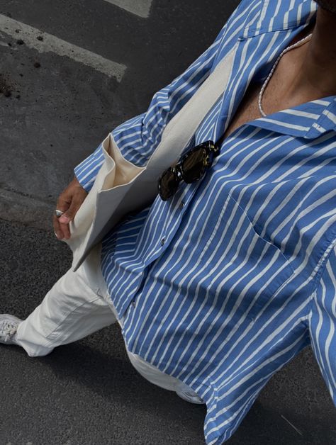 selfie from a bird’s eye view of a guy wearing a blue button up shirt with white vertical stripes, cream color baggy jeans, white sneakers and a cream color tote bag. Sunglasses, a chrome ring and an asymmetrical pearl necklace are used as accessories. Mens Blue Striped Shirt Outfit, Blue Button Up Outfit Men, Blue Shirt Outfit Men Aesthetic, Blue White Stripes Shirt Outfit, Blue Button Down Shirt Outfit Men, Blue And White Striped Shirt Outfit Men, Blue Longsleeves Outfit Men, Blue Button Up Shirt Outfit Men, Pinstripe Button Up Shirt Outfit