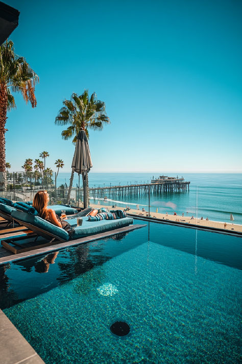 A woman relaxes on a poolside lounge chair with a stunning ocean view, overlooking a beach and pier in San Diego under a clear blue sky, one of the coolest places to stay in San Diego. San Diego Hotels, Floating Homes, Unique Places, Unique Hotels, Floating House, Vintage Vibes, Hidden Gems, The List, San Diego