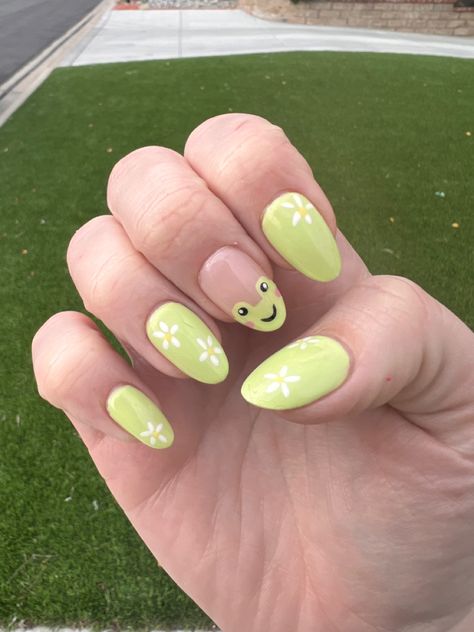 Green grass background. Picture of right hand showing light green nails with white flowers. One fingernail has a drawing of a cartoon frog with blush. Simple Frog Nails, Frog Nail Art Designs, Animal Inspired Nails, Frog Nail Ideas, Animal Themed Nails, Frog Nails Acrylic, Frog Nails Designs, Raccoon Nails, Cute Animal Nails