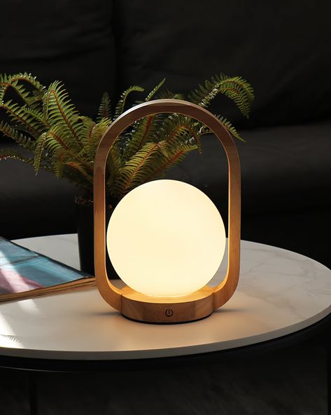 The Audo Wooden Portable Table Lamp is a beacon of serenity, elegantly crafted to bring a tranquil glow to any room. Its design features a smooth wooden arch, encircling a frosted globe that diffuses light into a soft, comforting embrace. Ideal for creating an atmosphere of calm and warmth, this lamp is not just a lighting solution but a piece of decor that complements a peaceful and modern aesthetic.   Purchase Notes:  Only supports shipping to Japan, Australia, the EU, and the United States, a Japandi Table, Japandi Lighting, Japandi Lamp, Portable Table Lamp, Wooden Arch, Energy Efficient Design, Portable Table, Color Changing Lights, Table Lamp Design