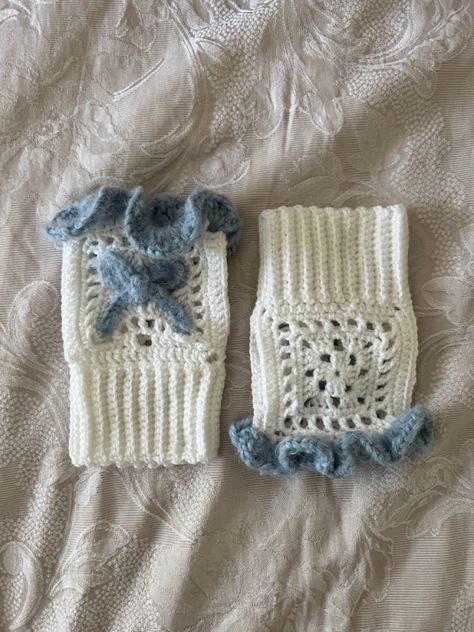 a pair of crocheted fingerless gloves lay next to each other on a beige jacquard weave quilt cover. one is laying the right way round with the front showing while the other is upside down and has the back showing. the glove has a textured blue ruffle trim at the top and a blue bow in the front middle (made using the same yarn). the remainder of the glove is white and the body has a granny square like pattern. the wrist of the glove is ribbed. Hand Warmer Crochet Pattern, Cute Crochet Gloves, White Yarn Crochet Ideas, White And Blue Crochet, Fluffy Crochet Projects, Crochet Ideas Blue, Hand Warmers Crochet Pattern, Croquette Crochet, Light Blue Crochet Ideas