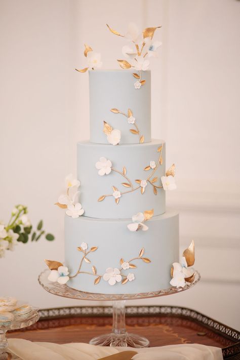 3 tier pale blue wedding cake with white molded sugar flowers and gold sugar vines and leaves decorating it on a clear glass pedestal cake plate. Blue Wedding Cake, Perfect Wedding Cake, Pretty Wedding Cakes, Dream Wedding Cake, Light Blue Wedding, Wedding Cakes Blue, Blue Themed Wedding, Blue Cakes, Simple Wedding Cake