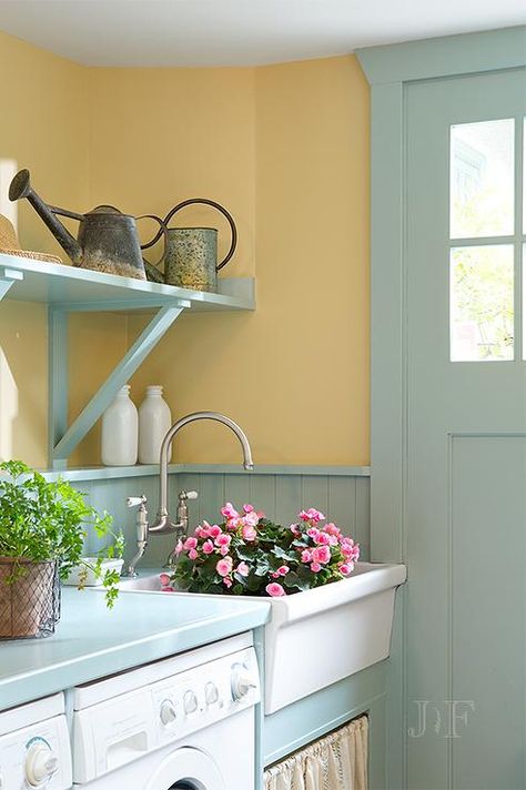 Turquoise mudroom features mustard yellow paint on upper walls and turquoise beadboard on lower walls lined with an enclosed washer and dryer as well as a white apron skirted sink under turquoise shelves. Yellow Mudroom, Blue Mudroom, Mustard Yellow Paint, Beadboard Trim, Cottage Laundry, Yellow Laundry Rooms, Cottage Laundry Room, Yellow Kitchen Walls, Laundry Room Storage Ideas