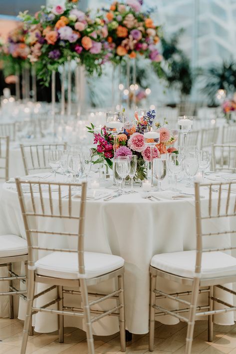 Vivid and bright colors fill the tables with this low style centerpiece on a round table. Colorful Round Table Wedding Decor, Floral Centrepiece Wedding Round Table, Wedding Table Centerpieces Round Tables, Round Table Decor Wedding, Round Wedding Table Decorations, Vibrant Centerpieces, Round Table Centerpieces Wedding, Centerpieces Round Table, Carnation Centerpieces