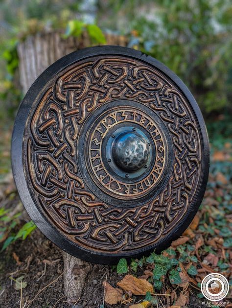 This shield's main decorative motif is a ring of Furhtrak Runes. Furthermore, the shield features a Viking-style braid and a metal boss. This model is made of 15mm thick birch plywood, finished with various stains ,linen seed oil, and acrylic-based varnish. The shield can be used as a decorative wall hanger or as a  functional piece for medieval reenactment or LARP. Size - 75 cm ( 29.5 inches ) in diameter  Weight - cca 5 kg  Material - 15 mm thick birch plywood Viking Shields, Viking Shield Cricut, Norse Shield, Viking Shield Design, Wooden Viking Shield Diy, Viking Home Decor, Celtic Shield, Handmade Gifts For Him, Viking Decor