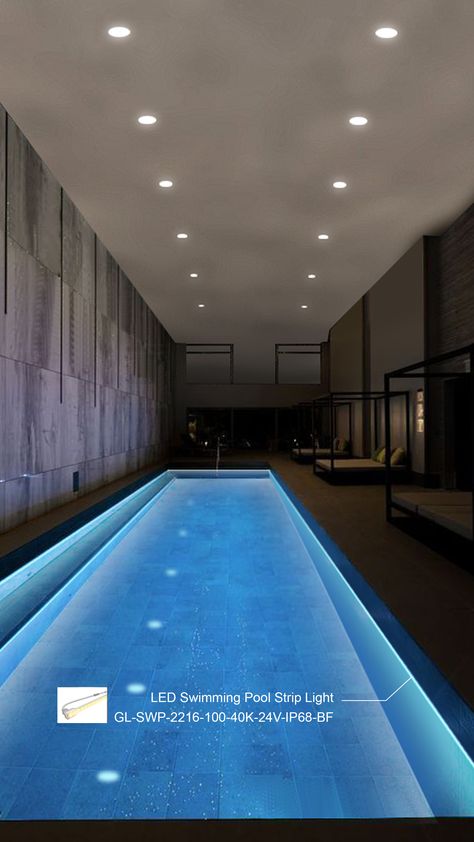 Elegant indoor swimming pool at night, featuring a vibrant blue LED strip light along the water's edge, model GL-SWP-2216-100-40K-24V-IP68-BF. The pool's surface sparkles under recessed ceiling lights that dot the textured gray ceiling. Concrete walls with vertical lines enhance the contemporary design. Large glass windows reveal relaxing lounge areas with daybeds and green cushions, adding a touch of comfort and luxury. Swimming Pool Led Strip Light, Indoor Pool Lighting, Floating Pool Lights, Perimeter Lighting, Led Pool Lighting, Swimming Pool Lights, Pool Lights, Swimming Pool Water, Recessed Ceiling Lights