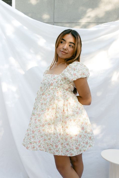 Our Pixie Dusted Dress is a mini cream babydoll dress with a small ditsy pink floral pattern. It displays a square neckline, slight puff sleeves, and subtle pleating throughout the bust for a fitted look. Has an adjustable back with a criss cross strapping detail. It also features a zipper closure for easy on and off access, fully lined, and a flowy babydoll fit below the bust. Has pockets too! Model wears a size x-smallModel is 5'2"100% Cotton / 100% Rayon Measurements:Bust: XS - 26" / S - 27" Cute Church Dresses, Floral Hoco Dress, Castle Collection, Hoco Inspo, Church Fits, Thrift Inspo, Amazon Dresses, Pink Floral Pattern, Cute Prom Dresses