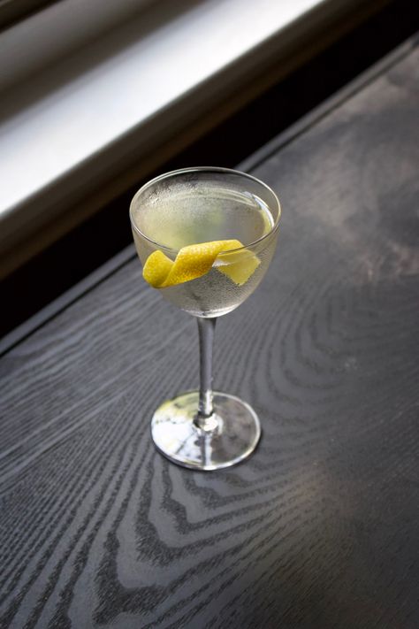 Picture of a Martini in a Nick & Nora glass, a stemmed glass with a short and small bowl. The drink itself it’s pretty clear and it has a lemon twist on the edge of the glass for garnish. It is sitting on black wood with a white window ledge in the background. Citrus Garnish, Orange Bitters, Drinks Recipe, Lemon Twist, Nick And Nora, Dry Vermouth, Cocktail Garnish, London Dry Gin, Cocktail Drinks Recipes