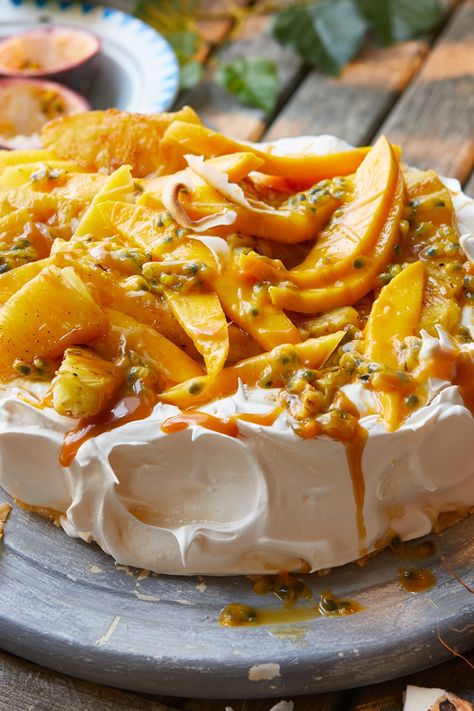 A pavlova base topped with mango slices, passion fruit seeds, roasted pineapple pieces and toffee sauce Tropical Fruit Pavlova, Mango Pineapple Dessert, Mango Pavlova Recipe, Pavlova Food Photography, Summer Pudding Recipe, Pavlova Tropical, Carribean Desserts, Tropical Pavlova, Passion Fruit Pudding