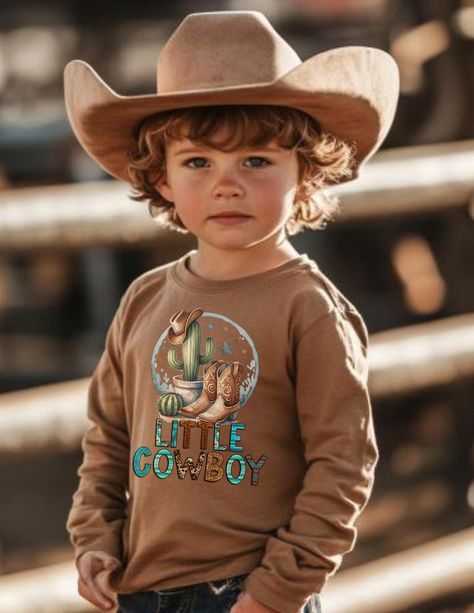 Yeehaw! Saddle up with our charming long sleeve boys' tee that celebrates the adventurous spirit of a 'Little Cowboy'.  It's a perfect addition to any young cowboy's wardrobe, inspiring them to embrace their adventurous side while showing off their love for the great outdoors! Let us be your go-to destination for all your kids' t-shirt needs! Our studio specializes in crafting fun, comfortable, and stylish t-shirts that kids will love to wear. Each shirt is made to order, ensuring a perfect fit and unique designs that cater to every child's personality. From vibrant colors to playful graphics, we have something for every little one. Trust us to provide high-quality, individually made t-shirts that your kids will cherish and proudly show off! We also have boutiques in Midlothian, Virginia & Country Kids Outfits, Midlothian Virginia, Playful Graphics, Western Clothes, Gift Sack, Fall Family Pictures, Little Cowboy, Country Kids, Cowboy Outfits