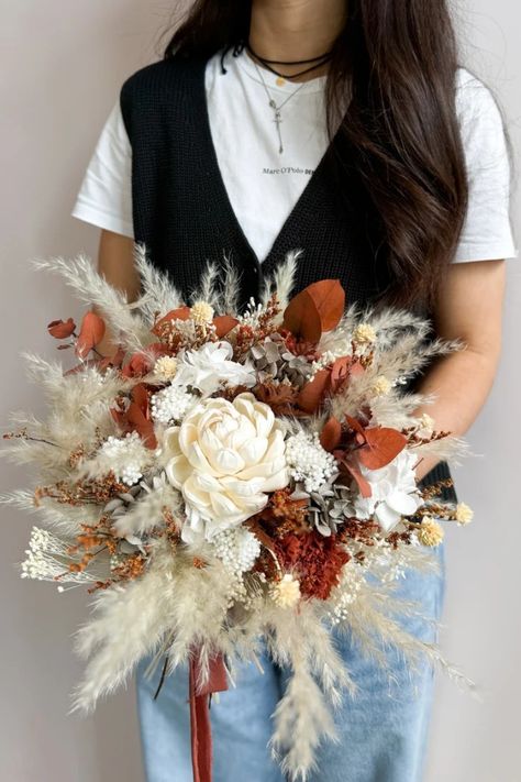 Your special day deserves a bouquet that reflects your free spirit and love for nature. This handcrafted boho bridal bouquet, bursting with warm terracotta, burnt orange, and sunshine yellow blooms, evokes the magic of autumn. Soft pampas grass adds a touch of texture, while luxurious cafe au lait roses whisper romance. Hand-tied with love, this bouquet is the perfect complement to your bohemian spirit and a forever memento of your rustic wedding celebration. Burnt Orange And Pampas Wedding Flowers, Burnt Orange Wedding Flowers, Dry Flower Bouquet, Boho Bridal Bouquet, Autumn Soft, Preserved Hydrangea, Preserved Eucalyptus, Boho Wedding Flowers, Preserved Roses